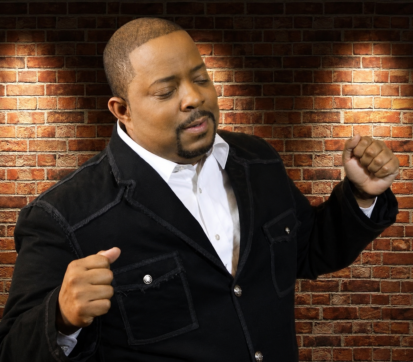 Pastor John Tillery in black blazer against brick wall — professional portrait