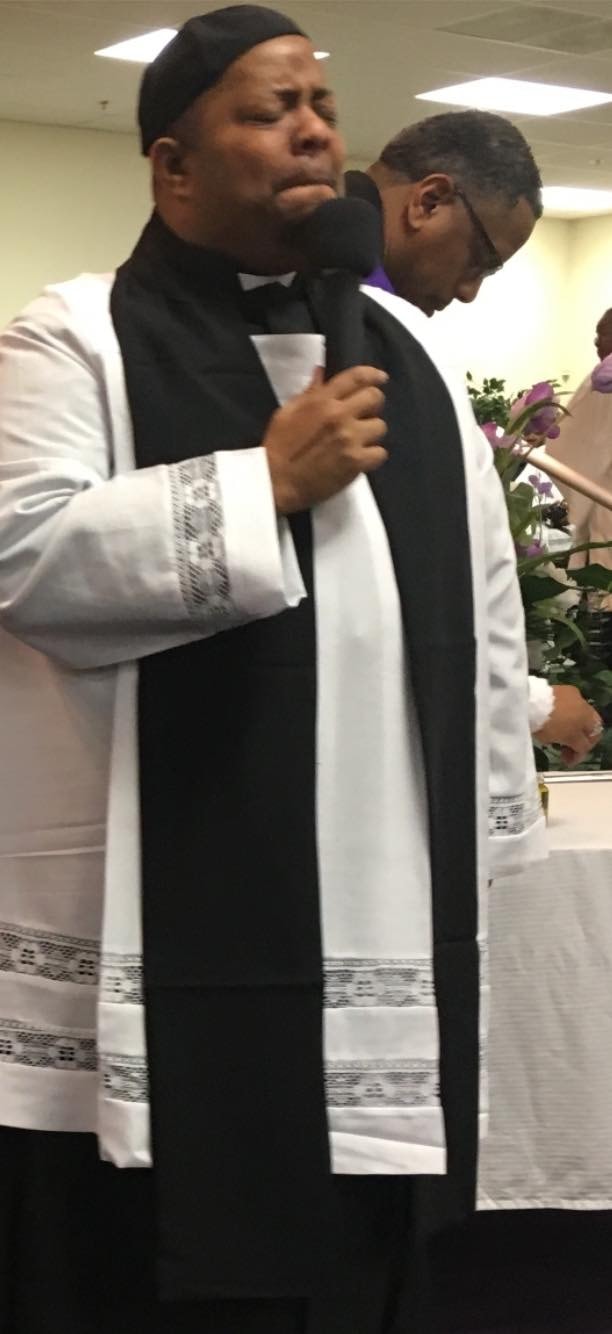 Pastor John Tillery singing at the microphone in clerical robes