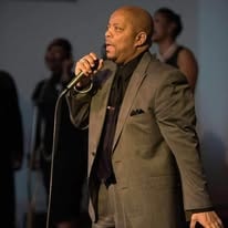 John Tillery singing on stage in tan blazer
