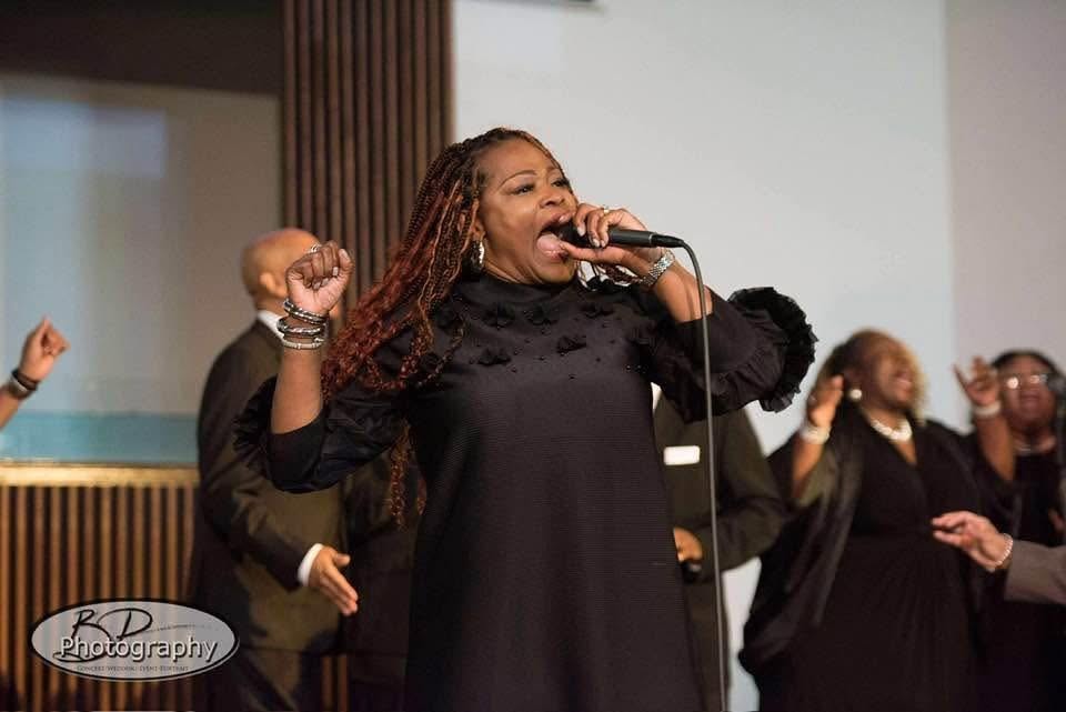 Lady Tillery singing passionately at microphone with choir behind her