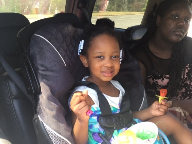 Young girl in car seat smiling with snacks