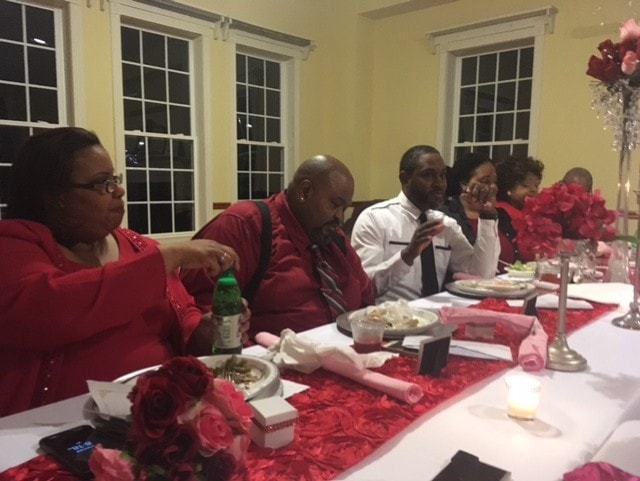 Group seated at formal dinner table with red roses and candles