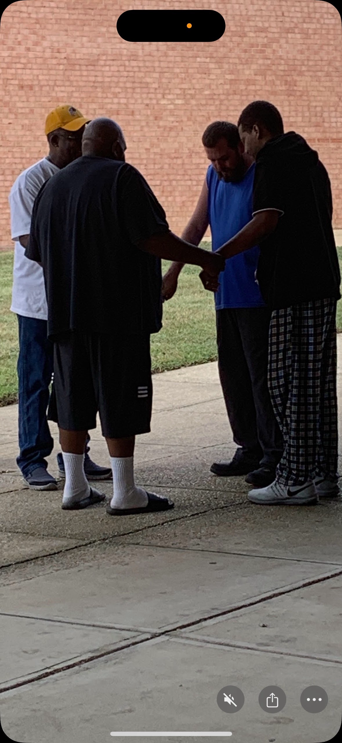 Four brothers praying together outside against brick wall