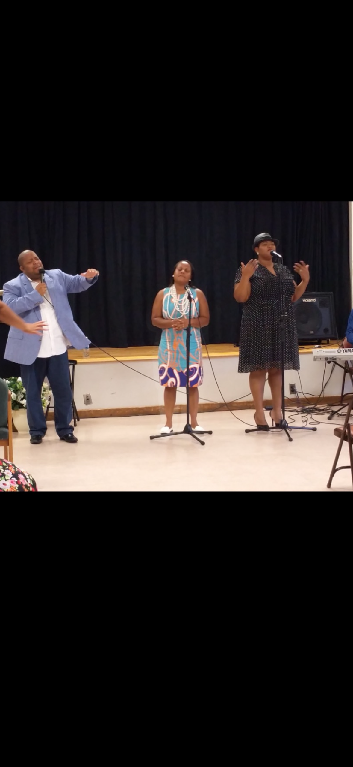 Three singers performing on stage with microphones and keyboard